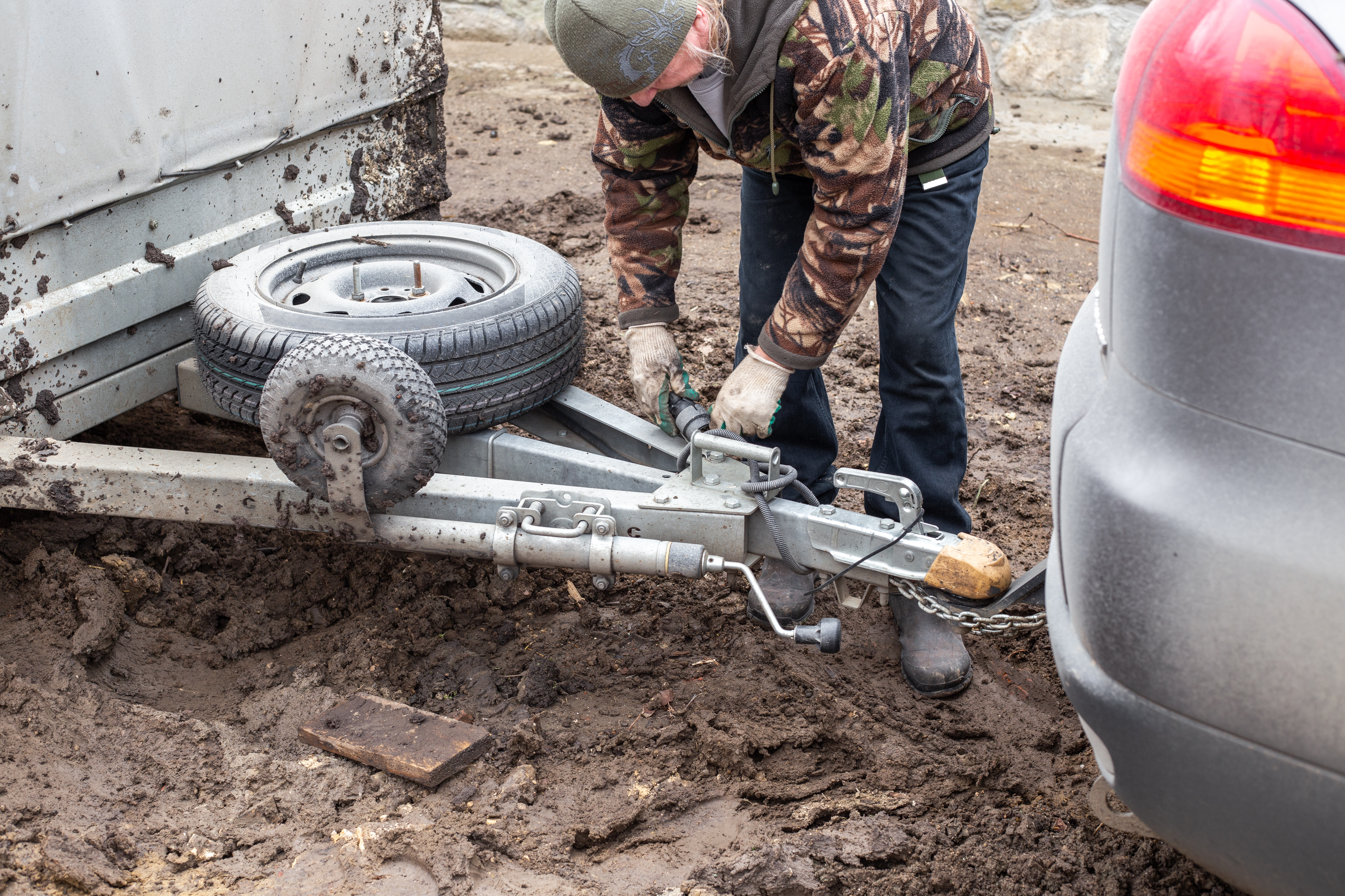 A person inspecting a trailer hitch while preparing to load heavy equipment, emphasizing safe loading techniques and proper trailer inspections.