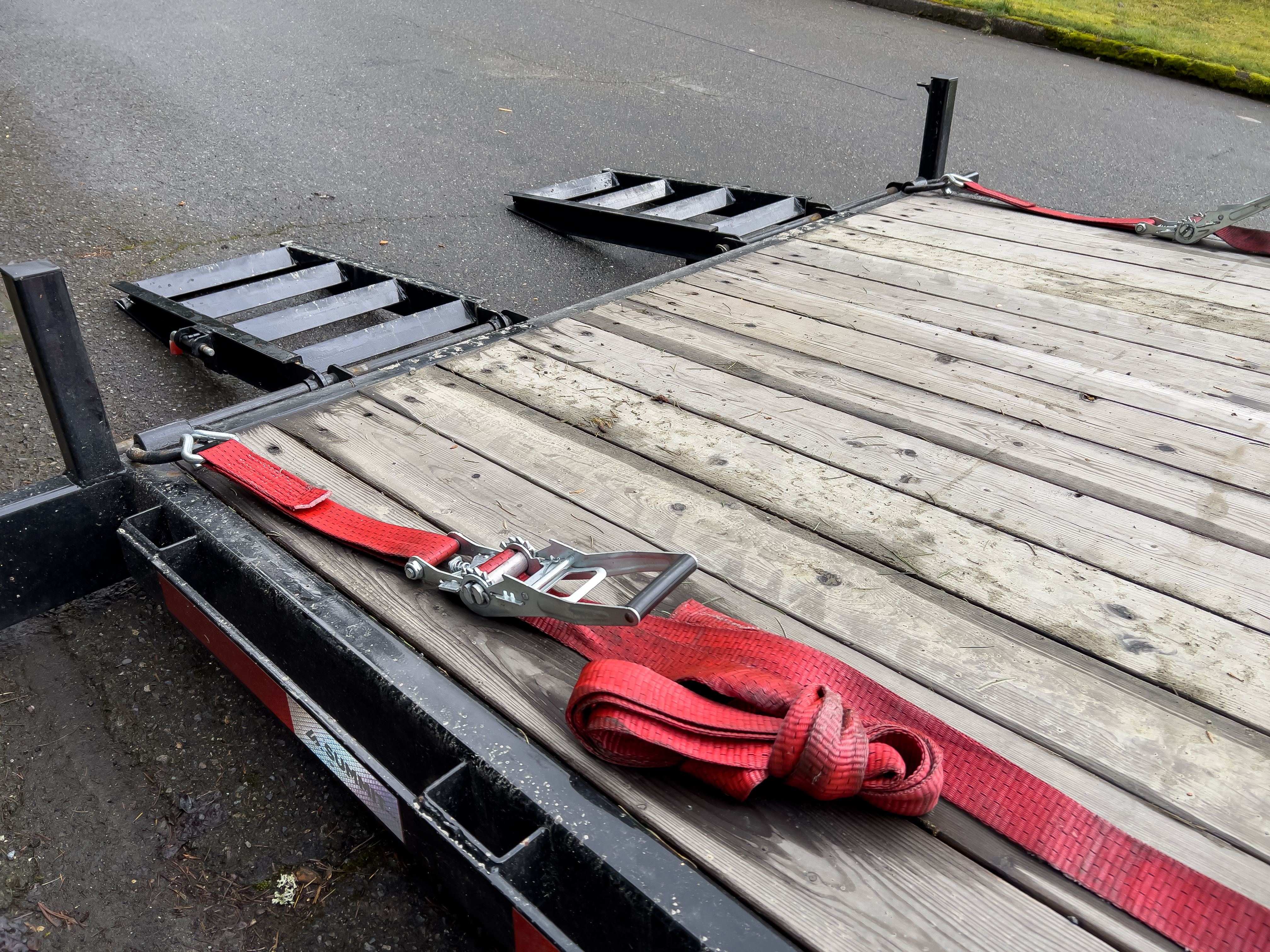 Close-up of a flatbed trailer with loading ramps and ratchet straps, illustrating safe loading techniques for heavy equipment transport.