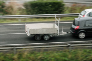 A car towing a small trailer on a highway, illustrating the importance of understanding trailer weight ratings, towing capacity, and safe towing practices.